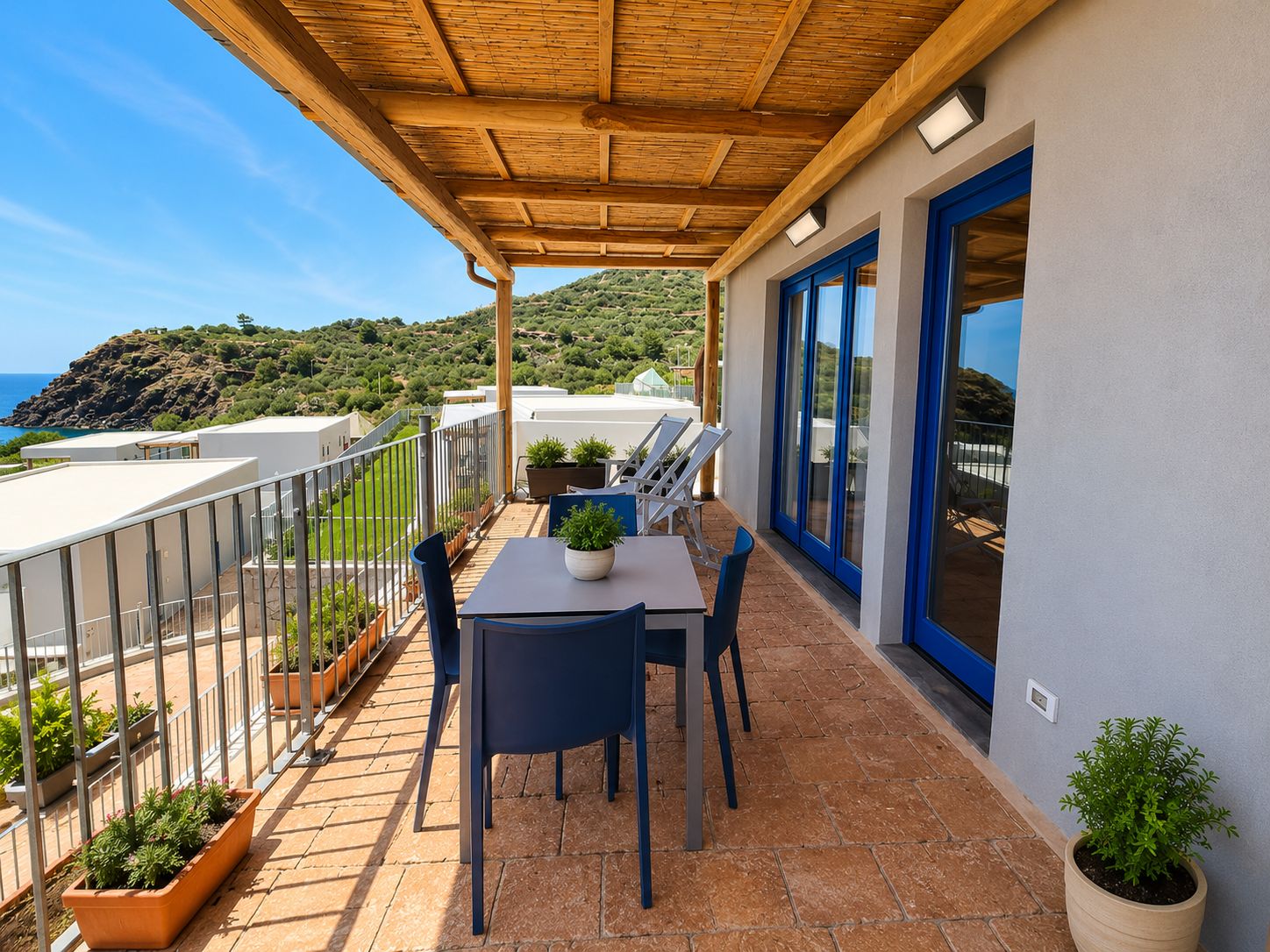 A terrace with a table and chairs, potted plants, and a view of the sea.