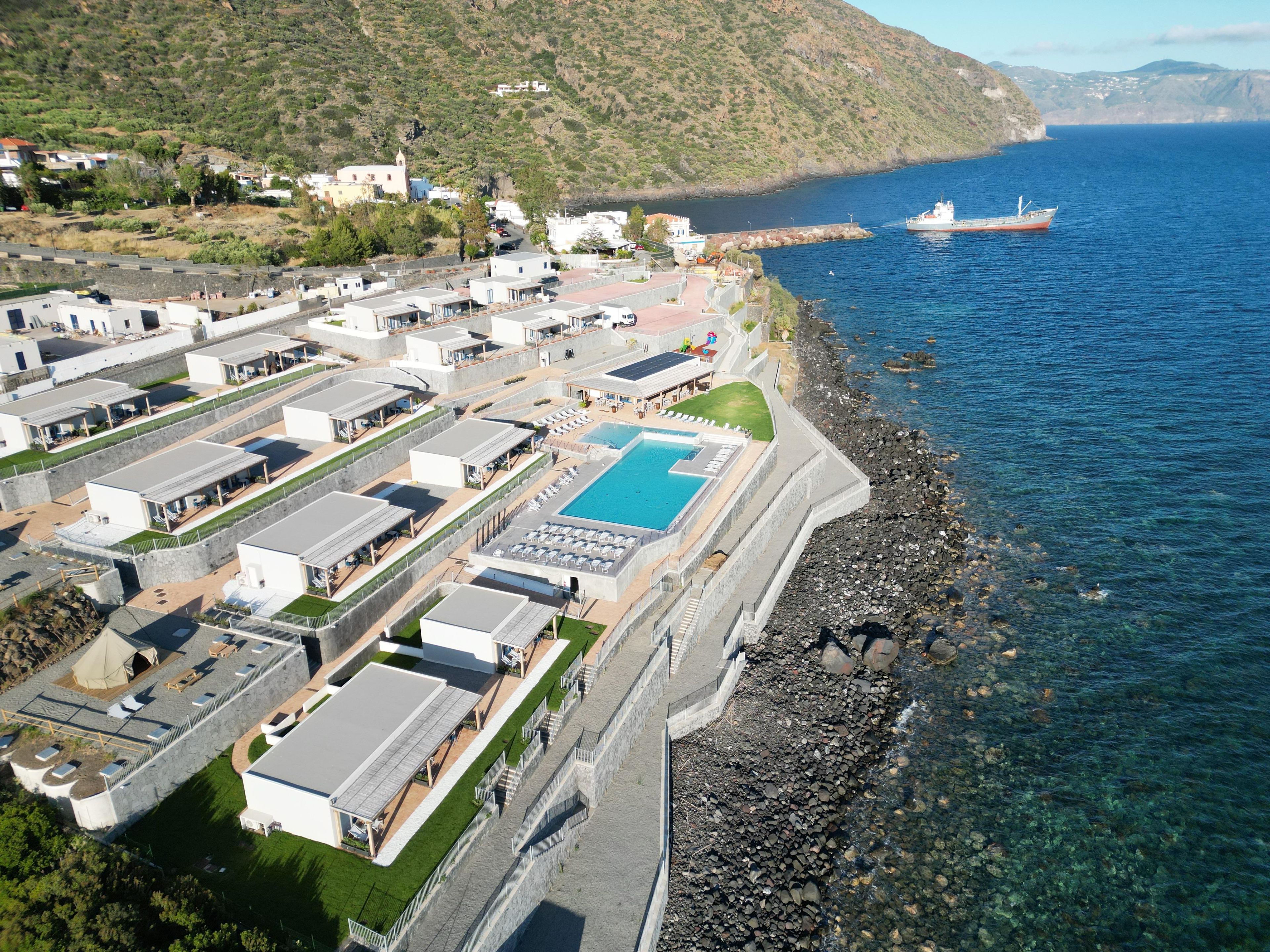 A coastal resort with multiple buildings, a swimming pool, and a rocky shoreline.