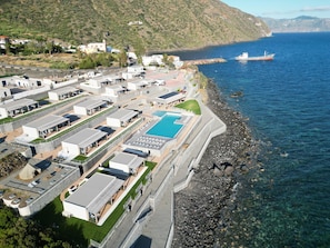 Un complejo turístico frente al mar con varias edificaciones, una piscina y un litoral rocoso.