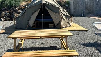 A tent with a picnic table in front, set on a gravel surface with a mountainous backdrop.