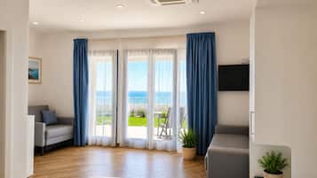 A hotel room with a bed, a sofa, a TV, and a balcony with a view of the sea.