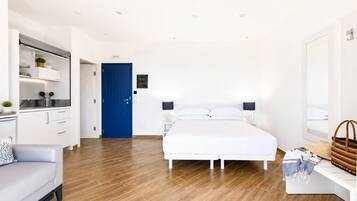 Una habitación de hotel moderna con piso de madera, una cama blanca, una puerta azul, un sofá blanco y un escritorio con una lámpara.