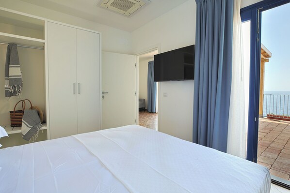 A hotel room with a bed, a wardrobe, a television, and a view of the sea.