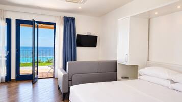 A hotel room with a bed, a sofa, a TV, and a balcony with a view of the ocean.