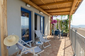 A balcony with a wooden pergola, two lounge chairs, a table with chairs, and a view of the sea.