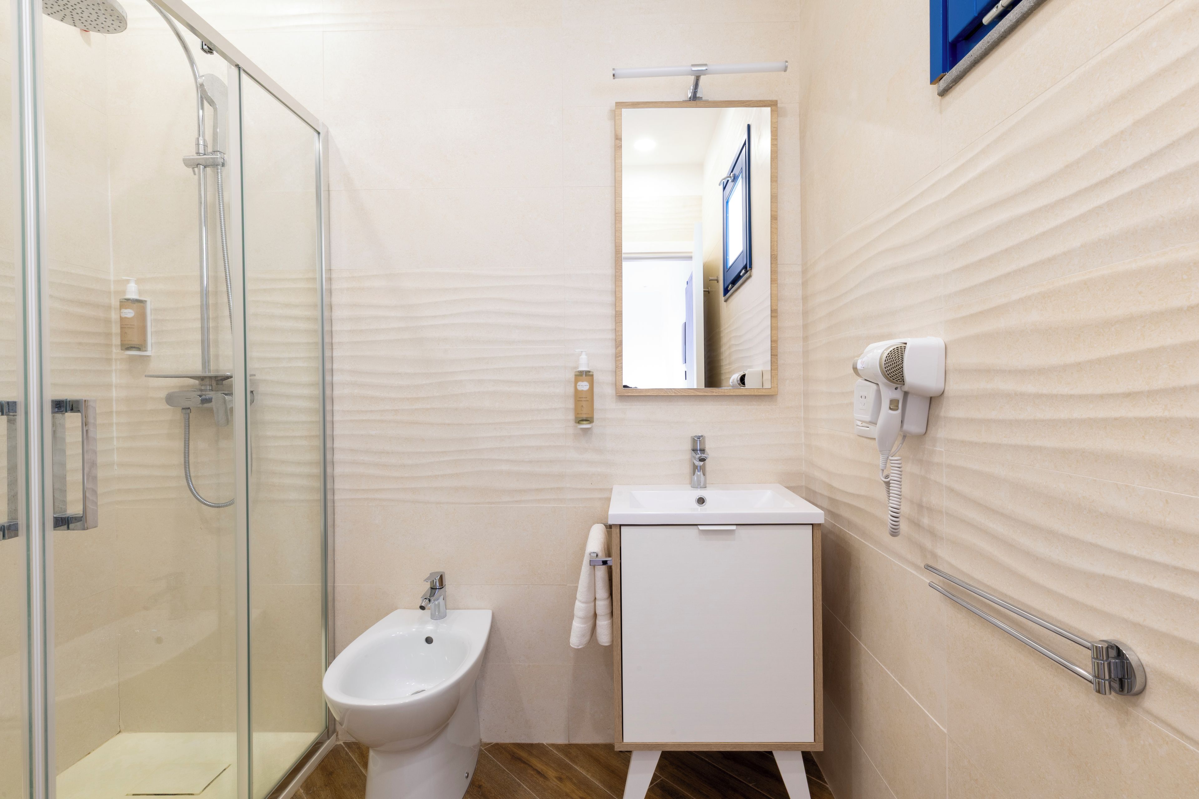 A bathroom with a glass shower enclosure, a white pedestal sink, and a mirror above the sink.