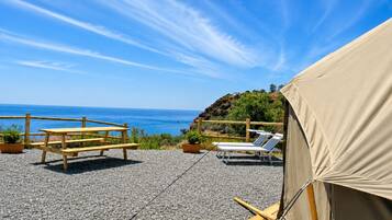 A beachside outdoor seating area with a wooden table and chairs, a covered tent, and a view of the ocean.