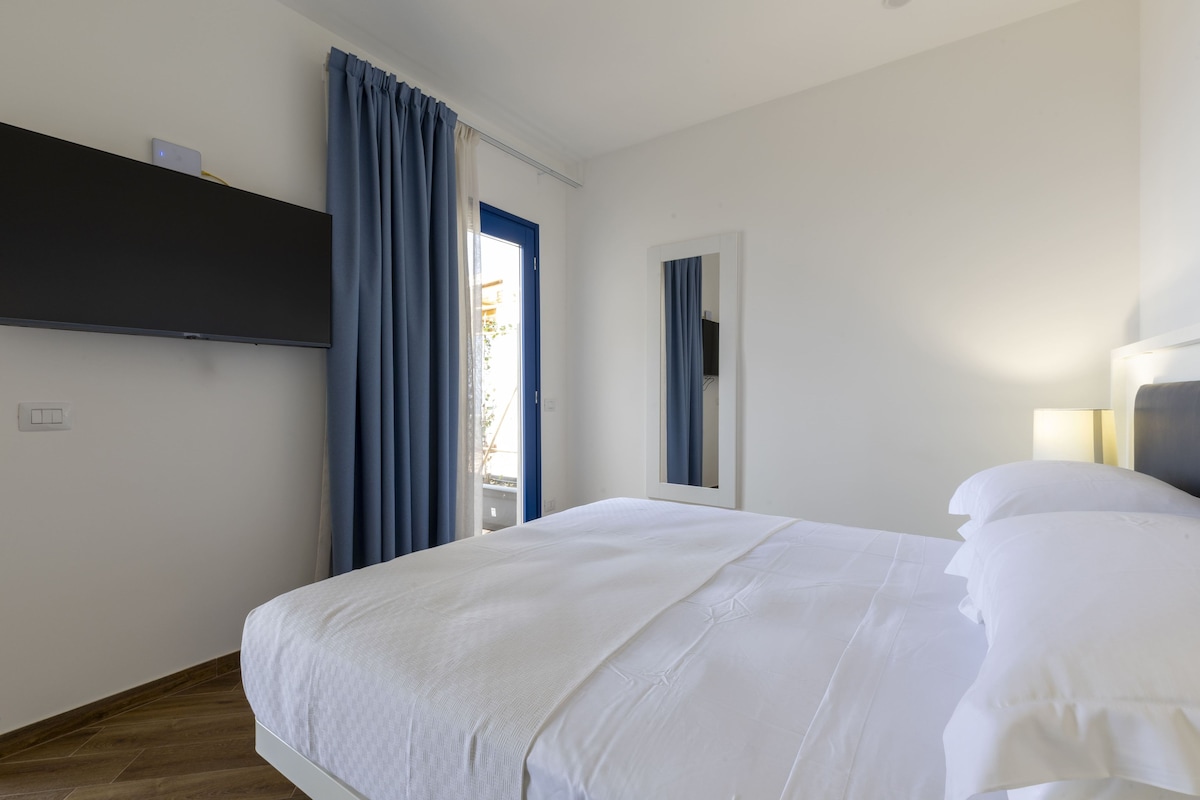 Habitación de hotel con cama, televisor de pantalla plana montado en la pared, una puerta con cortinas y una lámpara de noche.