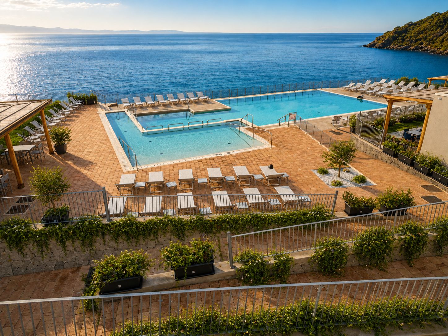 A pool area with multiple sun loungers and a view of the sea.