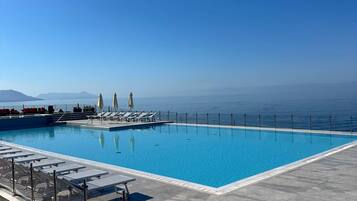 A clear blue pool with a view of the sea and mountains in the background.