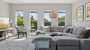 Una sala de estar moderna con un sofá seccional gris, un sillón negro, una mesita auxiliar, un televisor grande y una lámpara colgante.