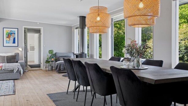 Un comedor moderno con una mesa grande, sillas negras y lámparas colgantes de mimbre.