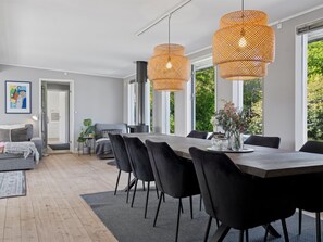 A modern dining area with a large table, black chairs, and wicker pendant lights.