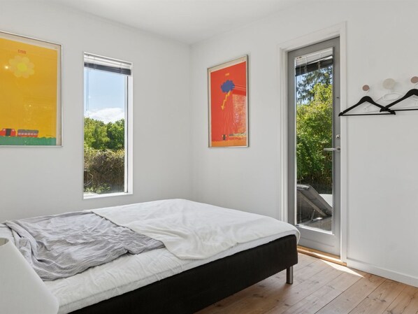 A modern bedroom with a bed, large windows, and a door leading to a balcony.