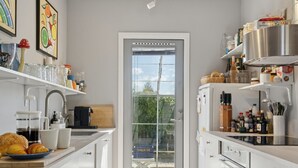 Una cocina moderna con armarios blancos, cafetera y vistas al exterior a través de un ventanal.