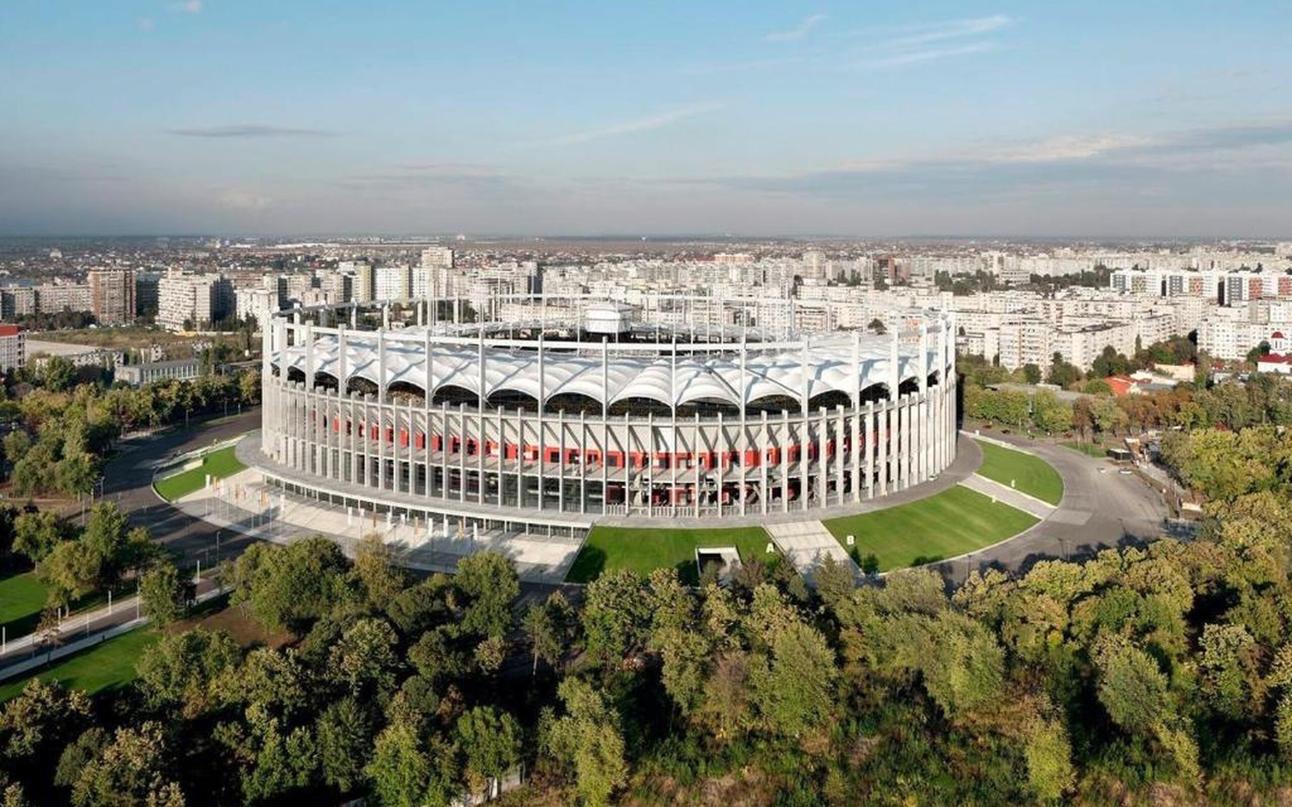 Ein Stadion mit kreisförmigem Design, umgeben von Stadtgebäuden und Grünflächen.
