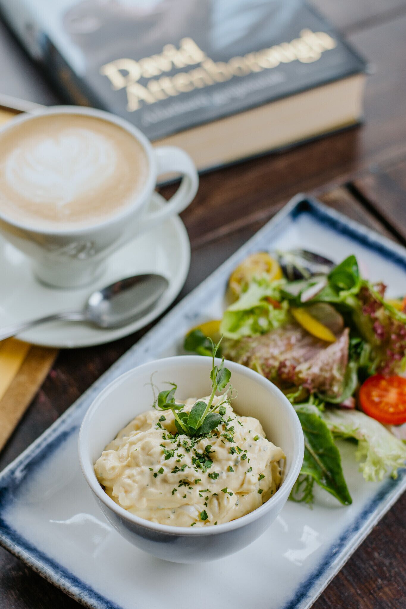 Una taza de café, un plato de comida y un libro sobre una mesa.
