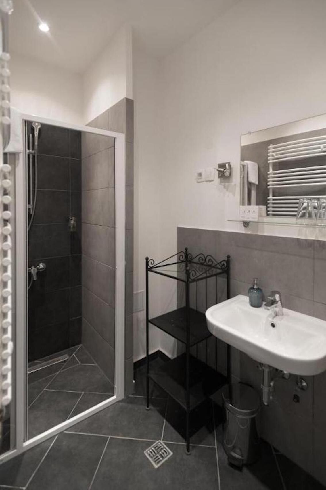 Un baño con ducha, un estante metálico negro, un lavabo y un espejo.