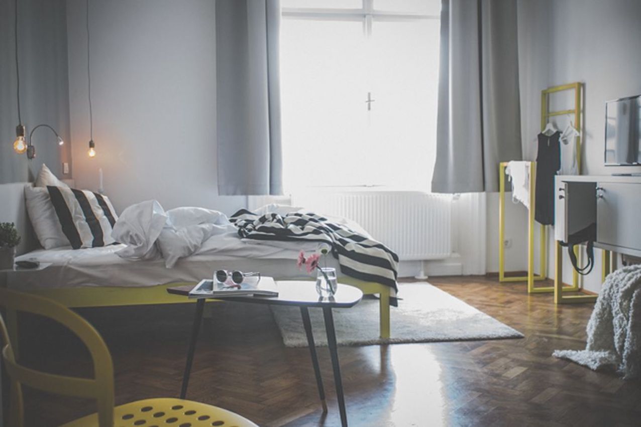 Een moderne hotelkamer met een bed, een klein tafeltje met dienblad, een stoel, een radiator, een televisie en een raam met gordijnen.