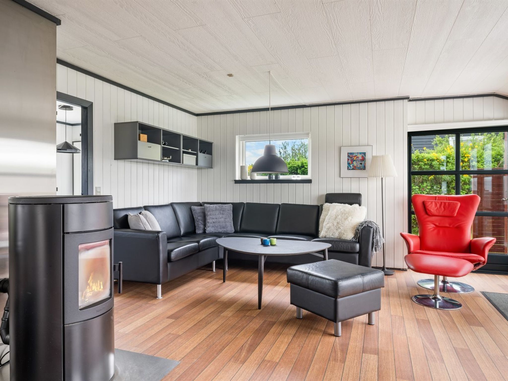 A modern living room with a sectional sofa, a round coffee table, a red chair, and a wood-burning stove.