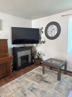 Un salon équipé d’un téléviseur à écran plat, d’une cheminée, d’une horloge et d’une table basse.