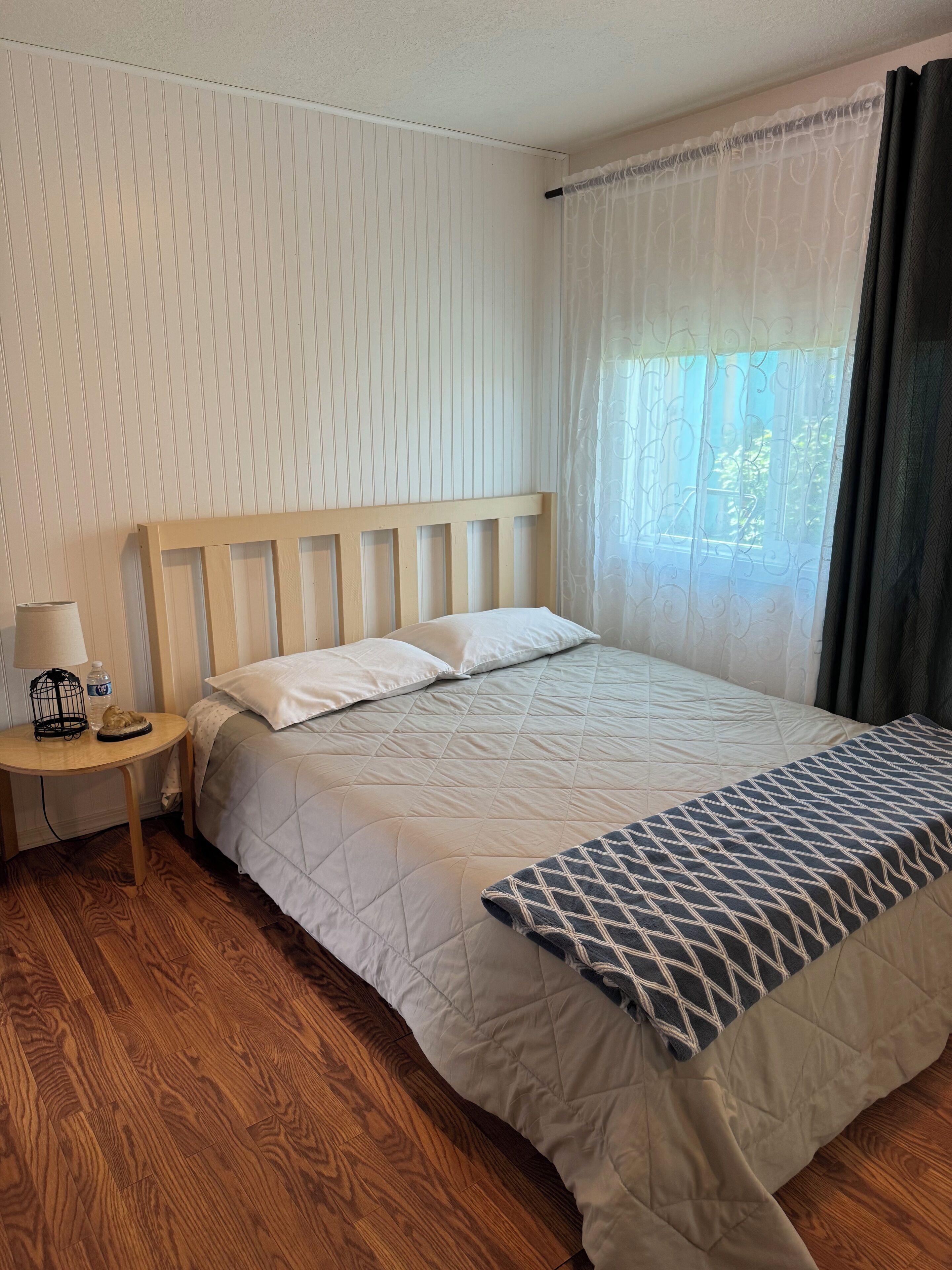 Un lit bien fait, avec une couverture matelassée, une tête de lit en bois et une table de chevet sur laquelle se trouvent une lampe et une bouteille.