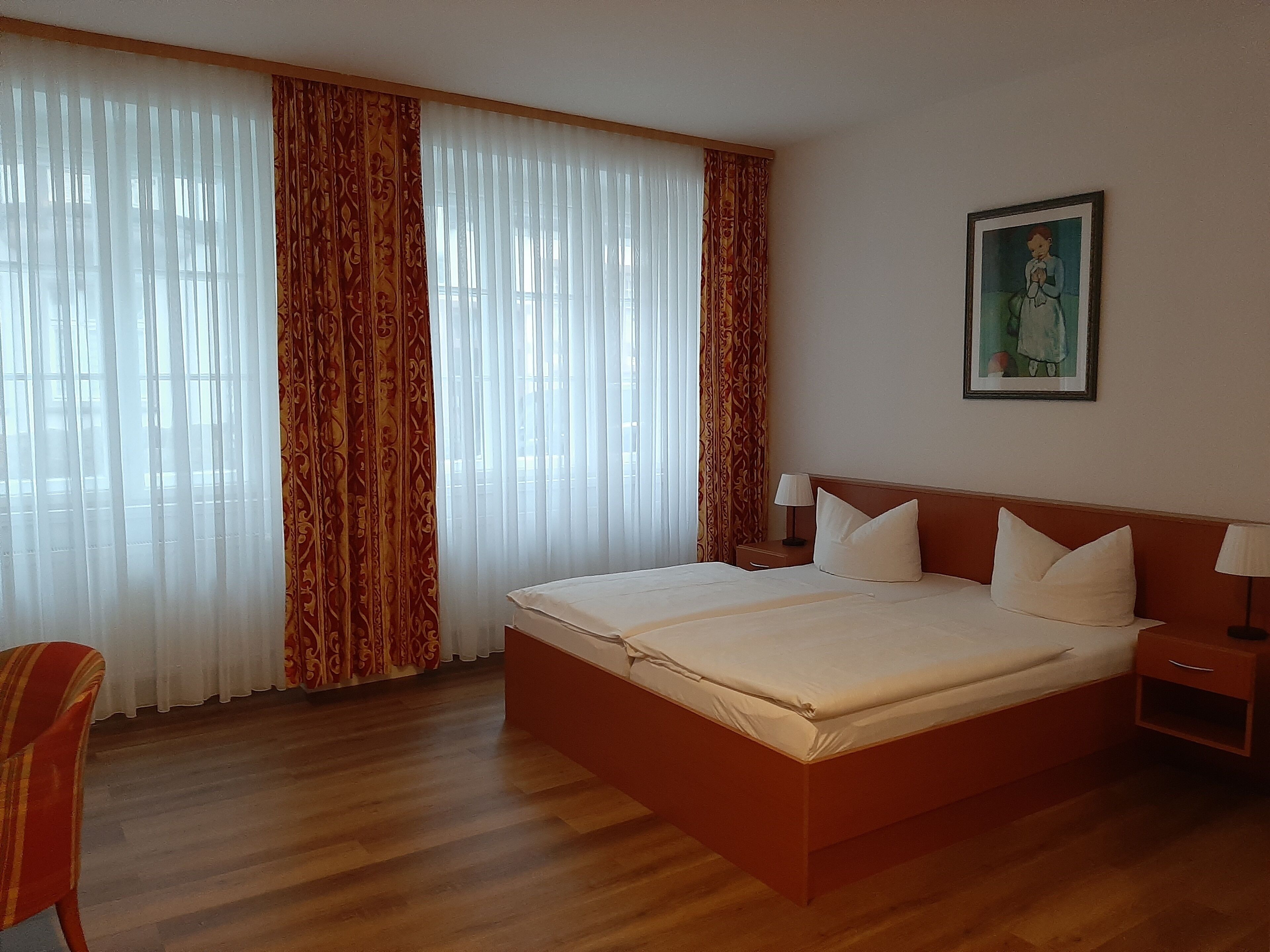 A hotel room with a large bed, wooden flooring, and curtains.