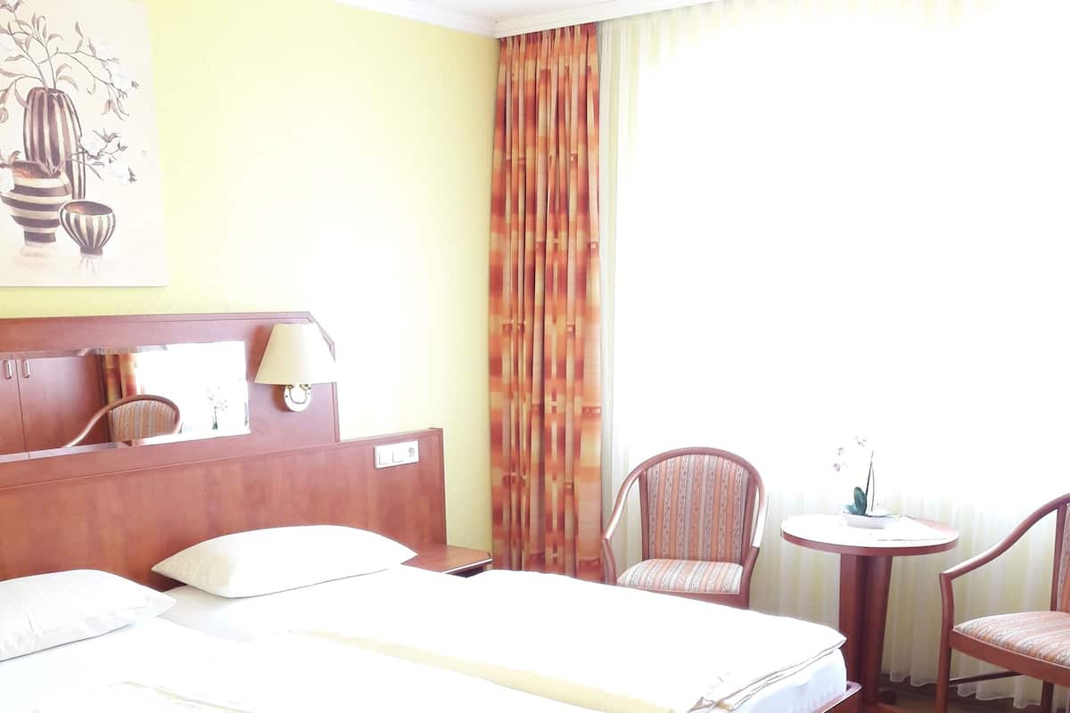 A hotel room with a large bed, two chairs, a small table, and a lamp.