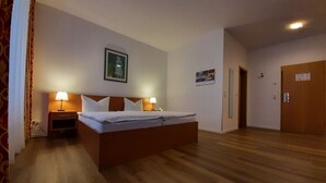 A hotel room with a large bed, two bedside tables with lamps, a wooden headboard, a painting on the wall, and a door to the right.