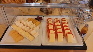 A buffet with various cheeses and sliced tomatoes on white plates.