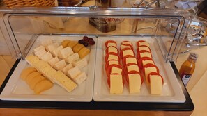 A buffet with various cheeses and sliced tomatoes on white plates.