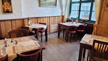 A restaurant with wooden tables and chairs, a large window with curtains, and hanging light fixtures.