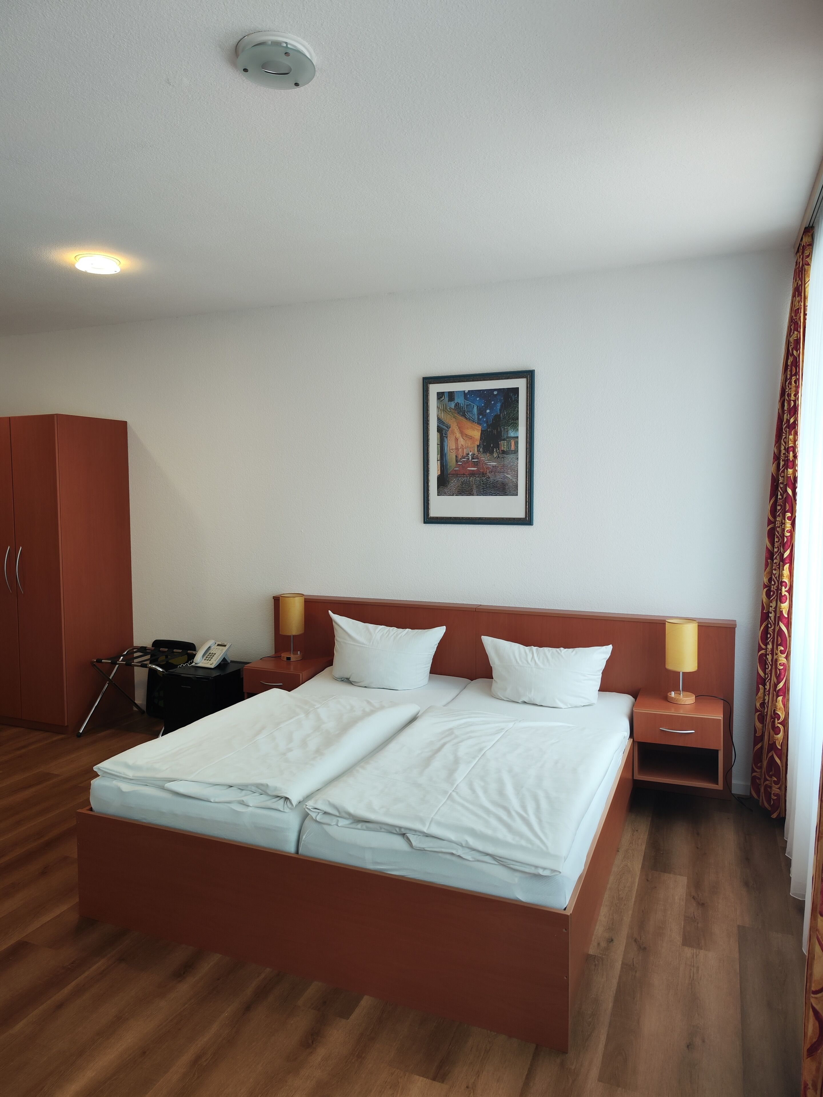 Een hotelkamer met een groot bed, een garderobe, een nachtkastje met een lamp, een telefoon en een schilderij aan de muur.