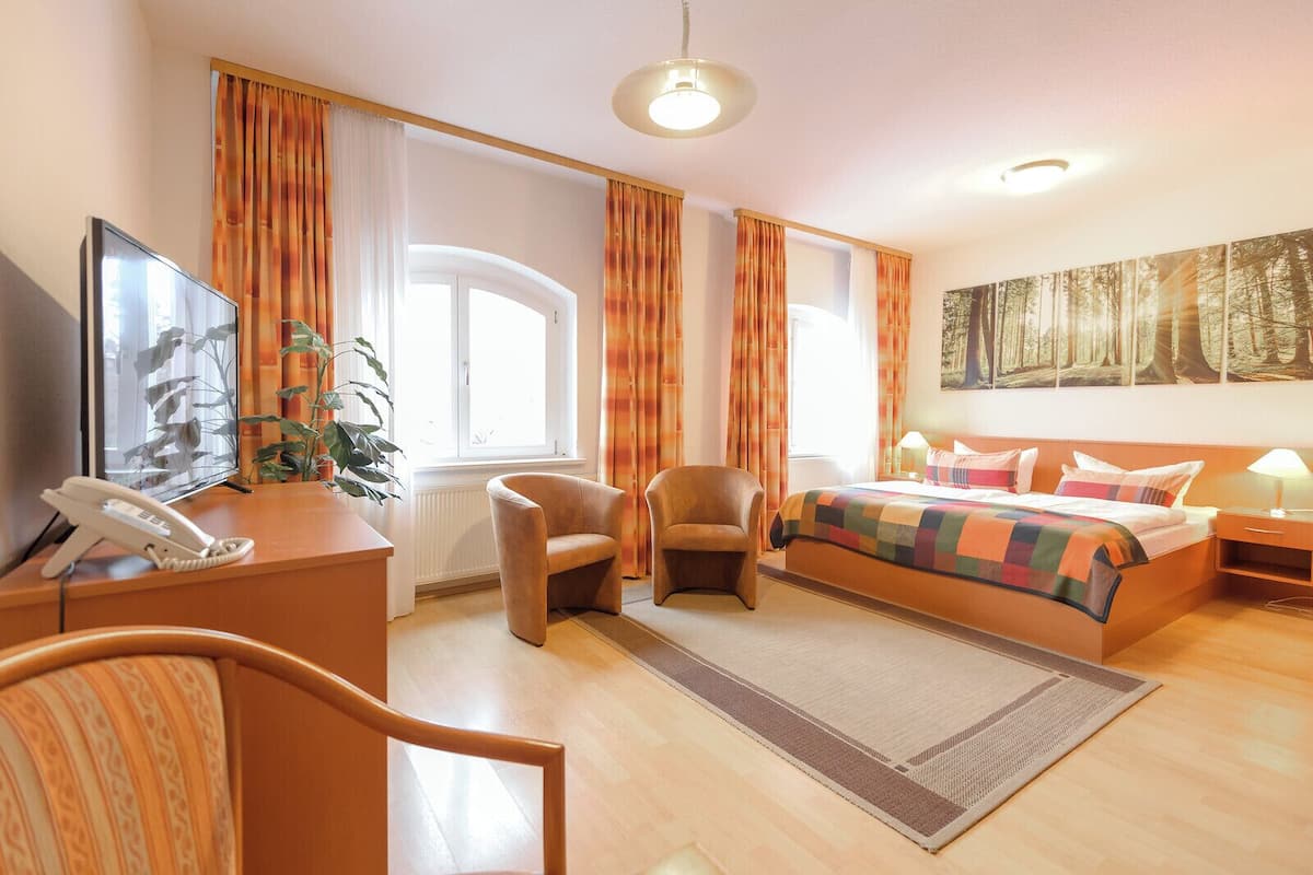 A hotel room with a bed, two armchairs, a desk with a telephone, and a large window.