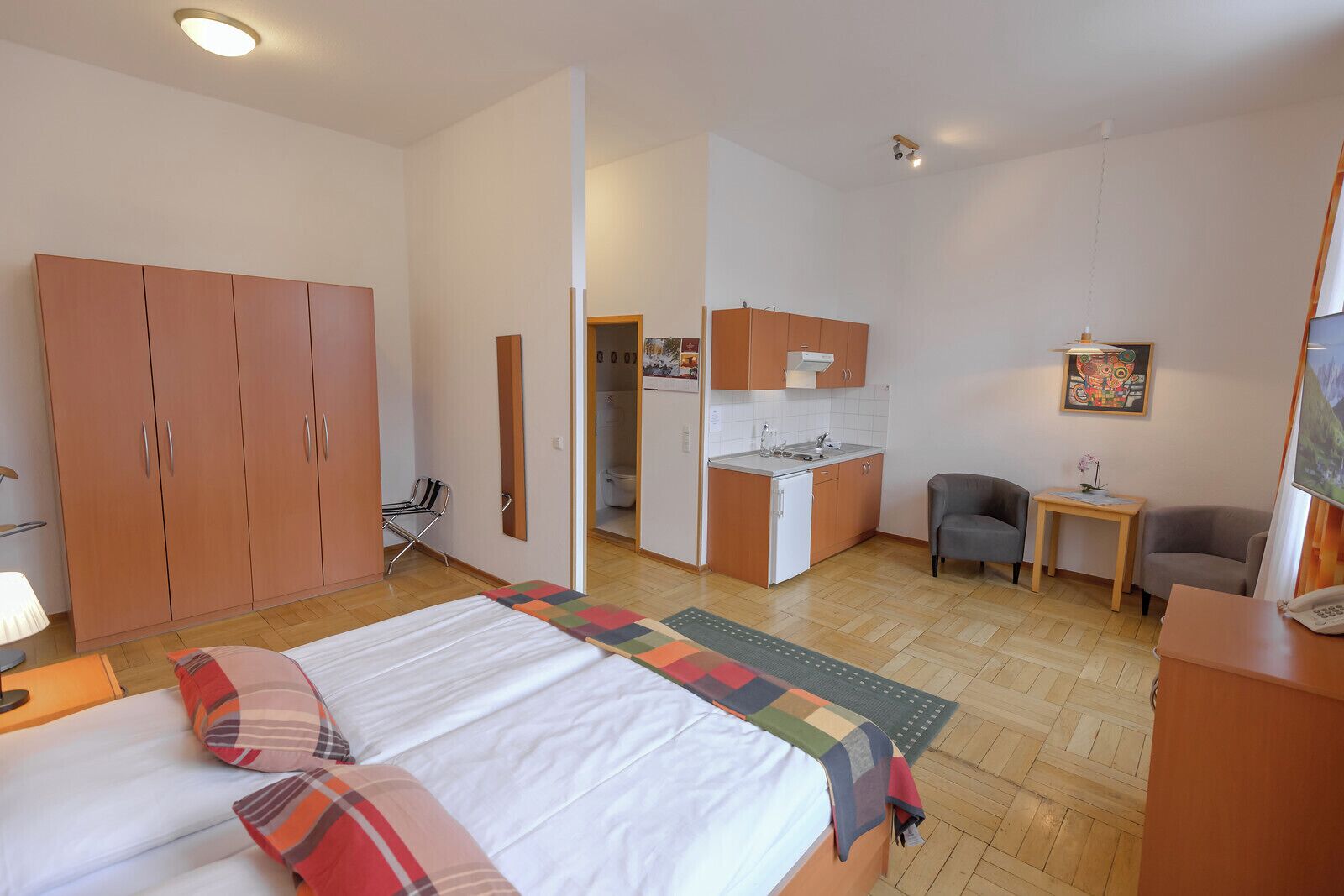 Una habitación de hotel con cama, escritorio, silla, kitchenette y armario.