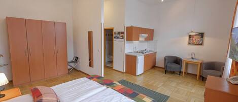 Una habitación de hotel con cama, escritorio, silla, kitchenette y armario.