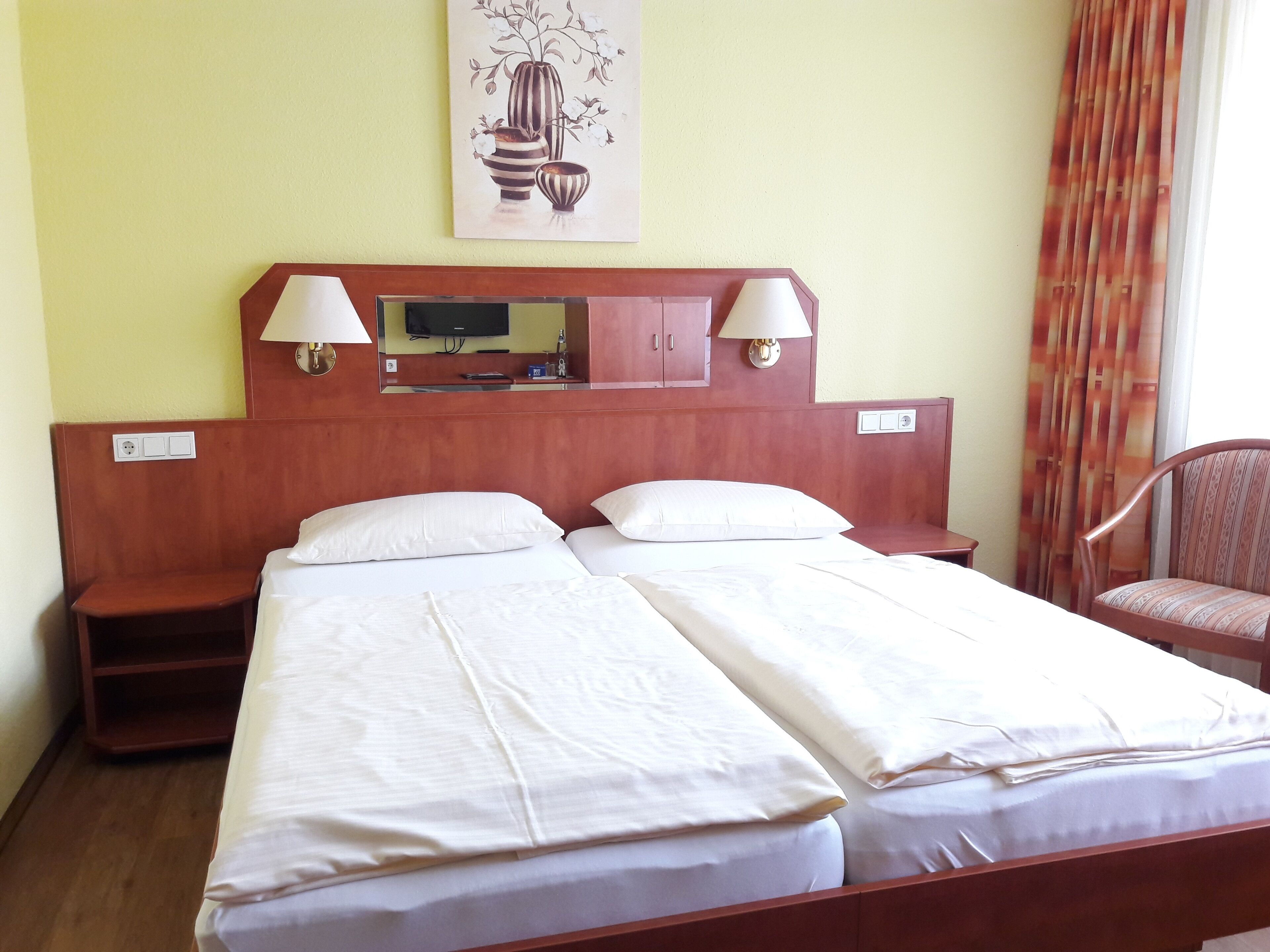 A hotel room with a double bed, two bedside tables, a TV, and a mirror above the bed.