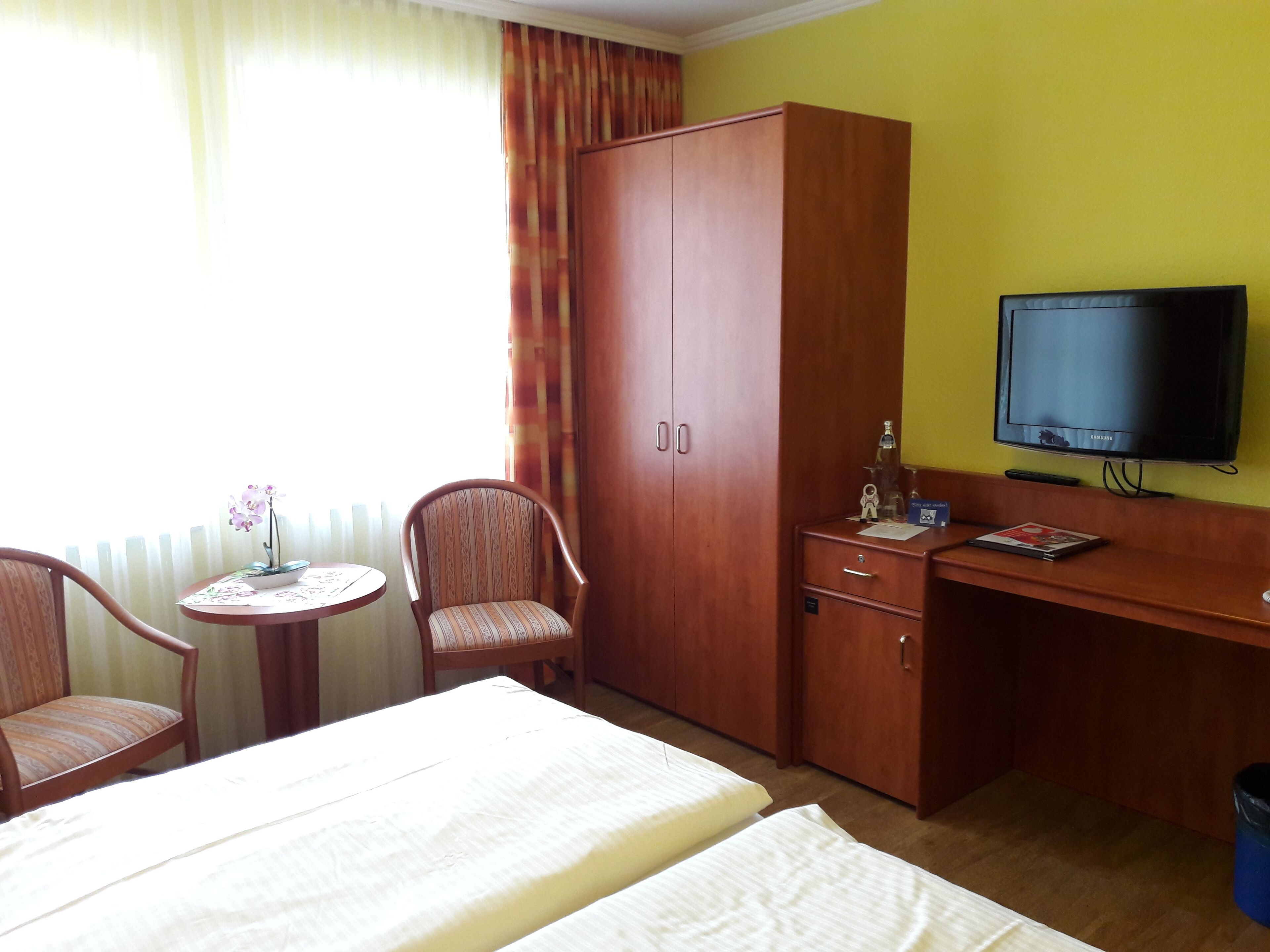 Una habitación de hotel con cama, escritorio con televisor, armario y dos sillas.
