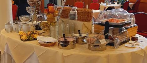 Een buffetopstelling met diverse gerechten en een koffiehoek, omringd door rode stoelen en een houten tafel.