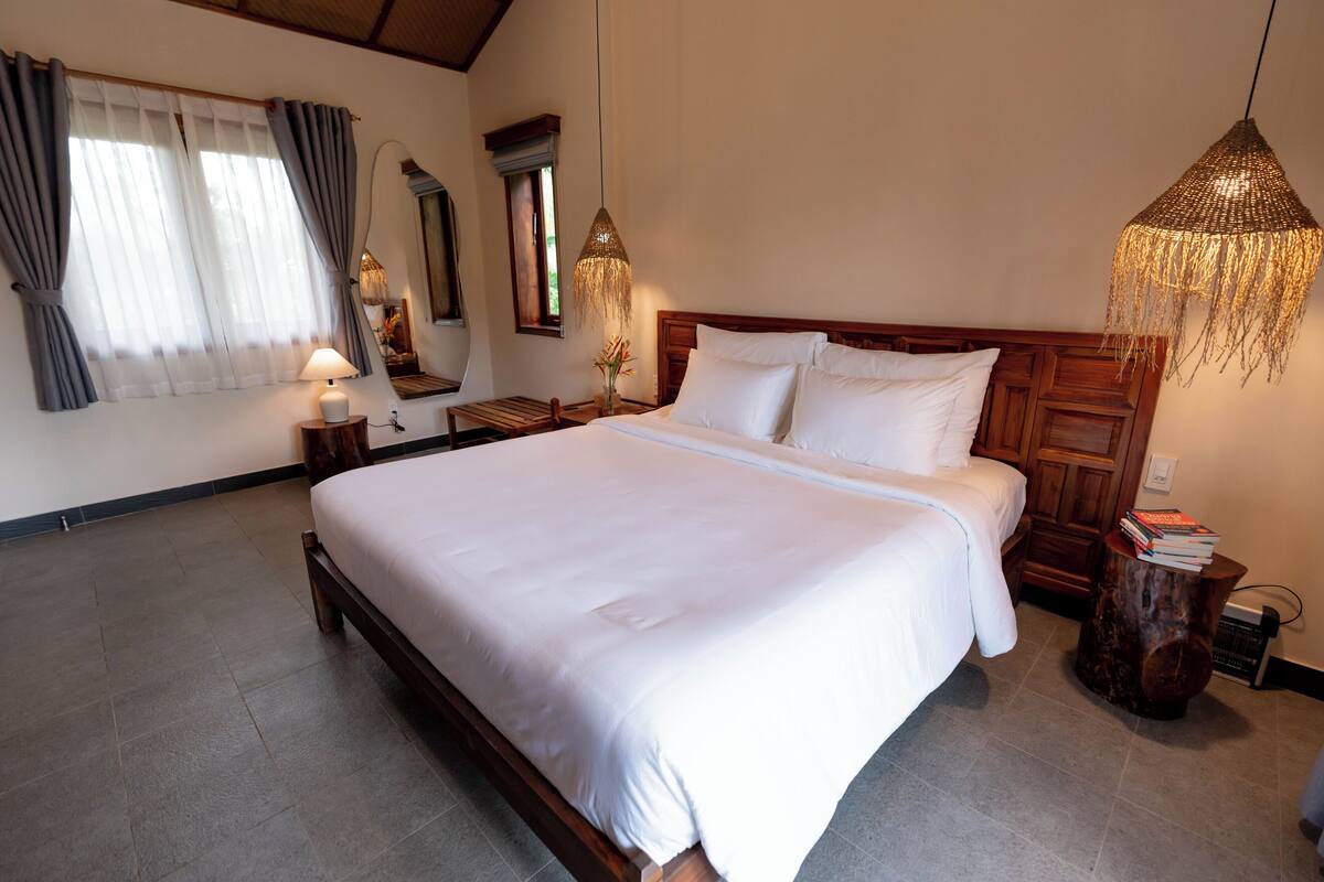 A neatly arranged bedroom with a large bed, bedside tables, a hanging light fixture, and a window with curtains.