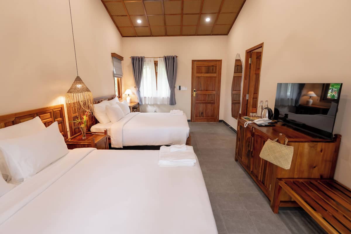 A hotel room with two beds, a wooden cabinet with a television, and a large window with curtains.