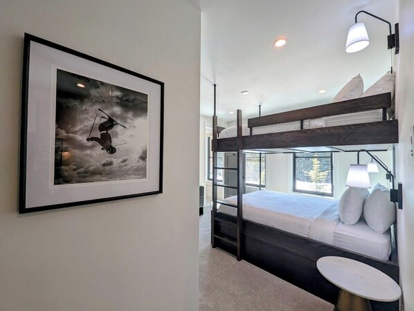 A bunk bed room with a framed picture on the wall, a bedside table, and a window with a view of trees. - Alcove 74 (Keystone)