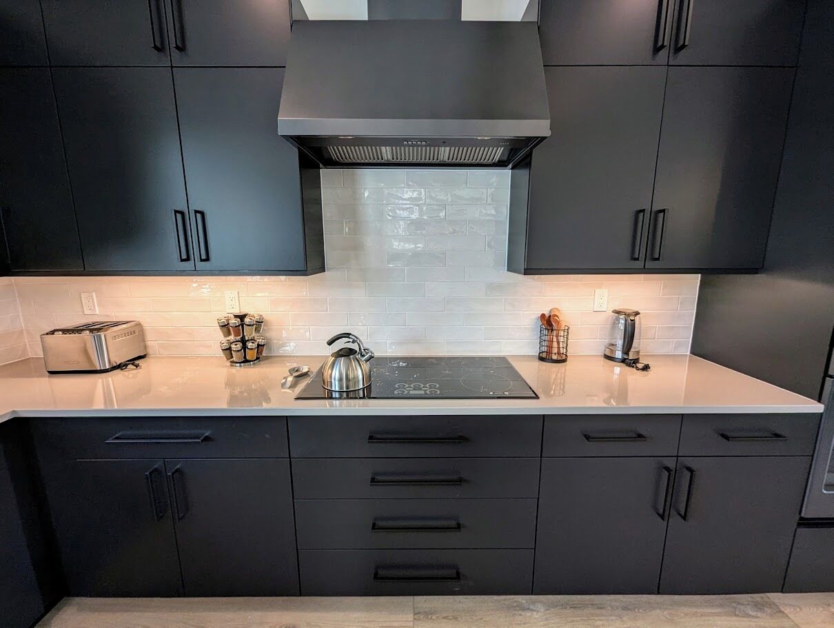 A modern kitchen with dark cabinets, a stainless steel kettle, and a built-in induction cooktop.