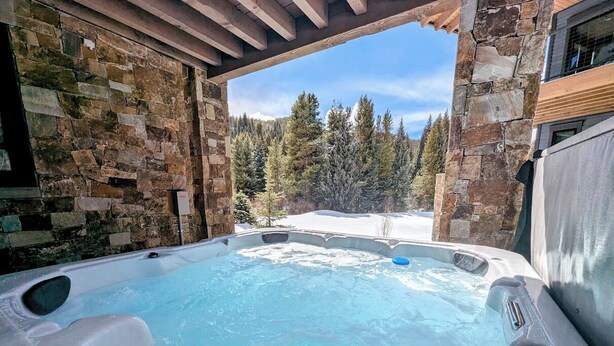 A hot tub with stone walls and a view of a snowy forest. - Alcove 74 (Keystone)