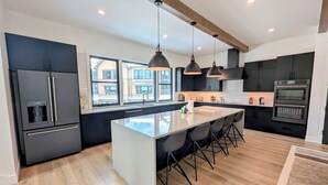 A modern kitchen with a central island, black cabinetry, stainless steel appliances, and pendant lighting. - Alcove 74 (Keystone)