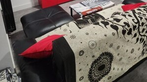 Una sala de estar con un televisor de pantalla plana montado en la pared, un mueble rojo, un sofá con un cojín estampado y una revista sobre la mesa de centro.