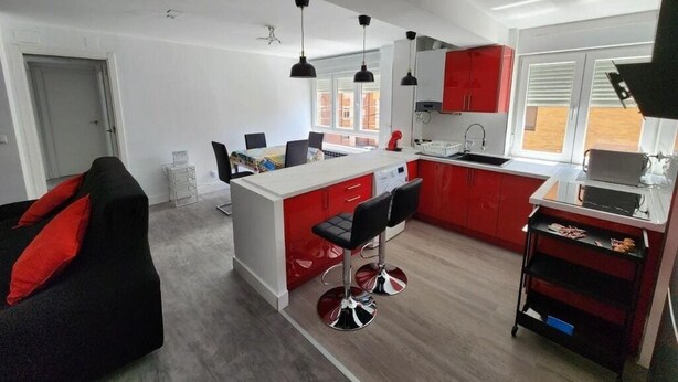 Una cocina moderna con gabinetes rojos, una isla central con taburetes altos e iluminación colgante.