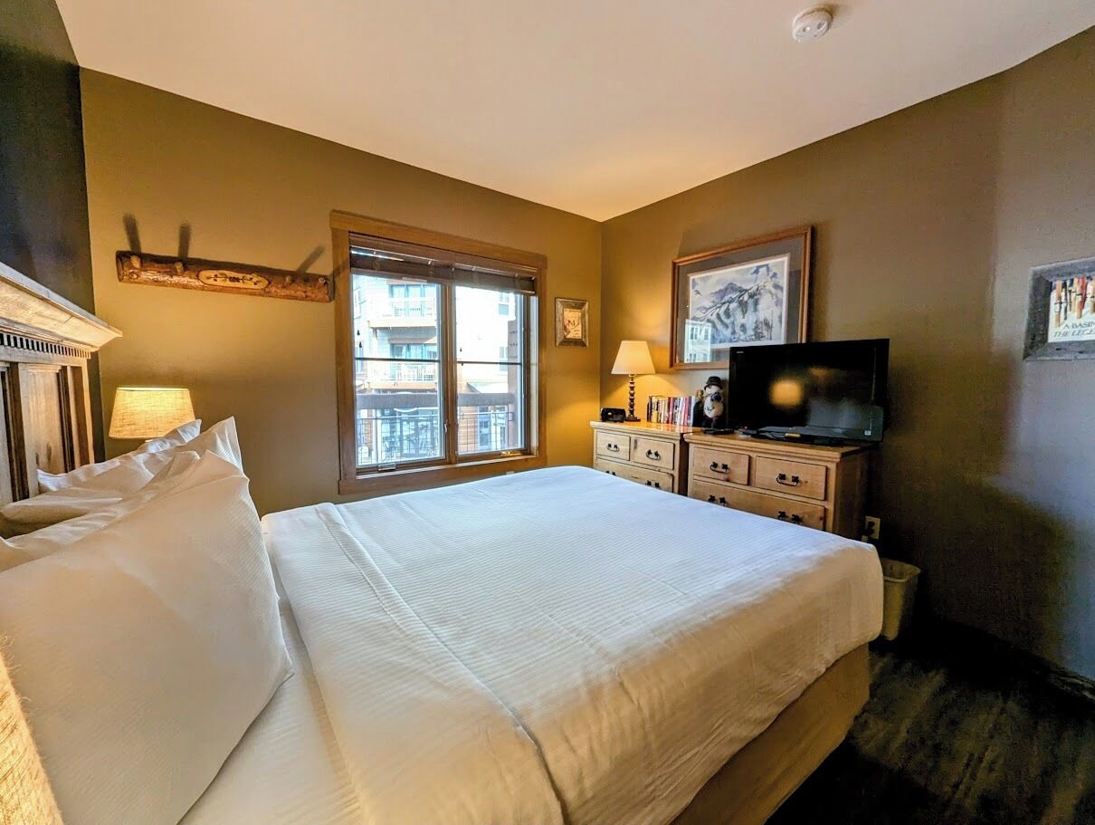 A hotel room with a large bed, a television, a window, and a dresser.
