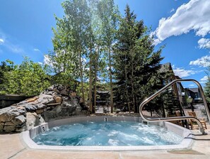 Ein Whirlpool, umgeben von Bäumen und einer Steinmauer, mit einer Metalltreppe, die zu einer Terrasse führt.