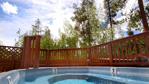 A hot tub with a wooden deck and a fence, surrounded by trees. - Trappers Crossing 8769 (Keystone)
